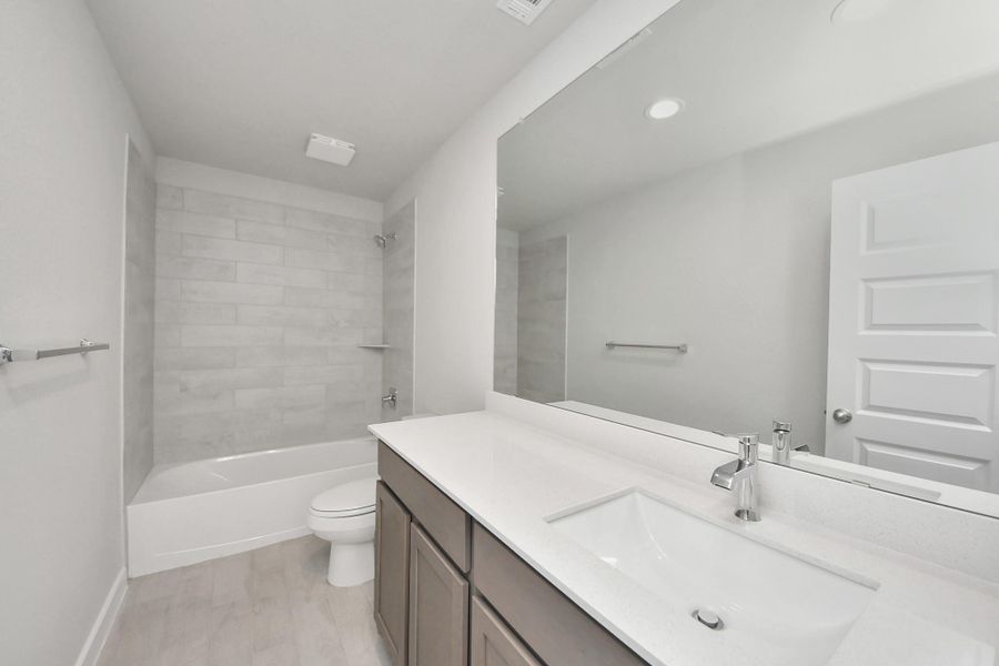 Secondary bath features tile flooring, bath/shower combo with tile surround, light stained wood cabinets, beautiful light countertop. Sample photo of completed home with similar floor plan. Actual colors and selections may vary.