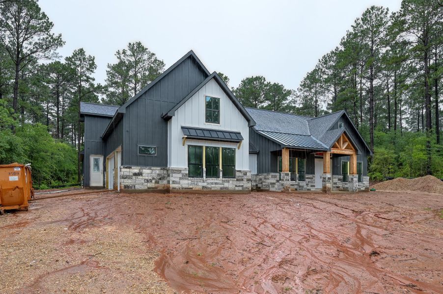 A modern, newly constructed home set in The Cedars community. This home features a combination of dark siding and stone accents, with a gabled roof and large windows. The lot is a spacious 1 acre.