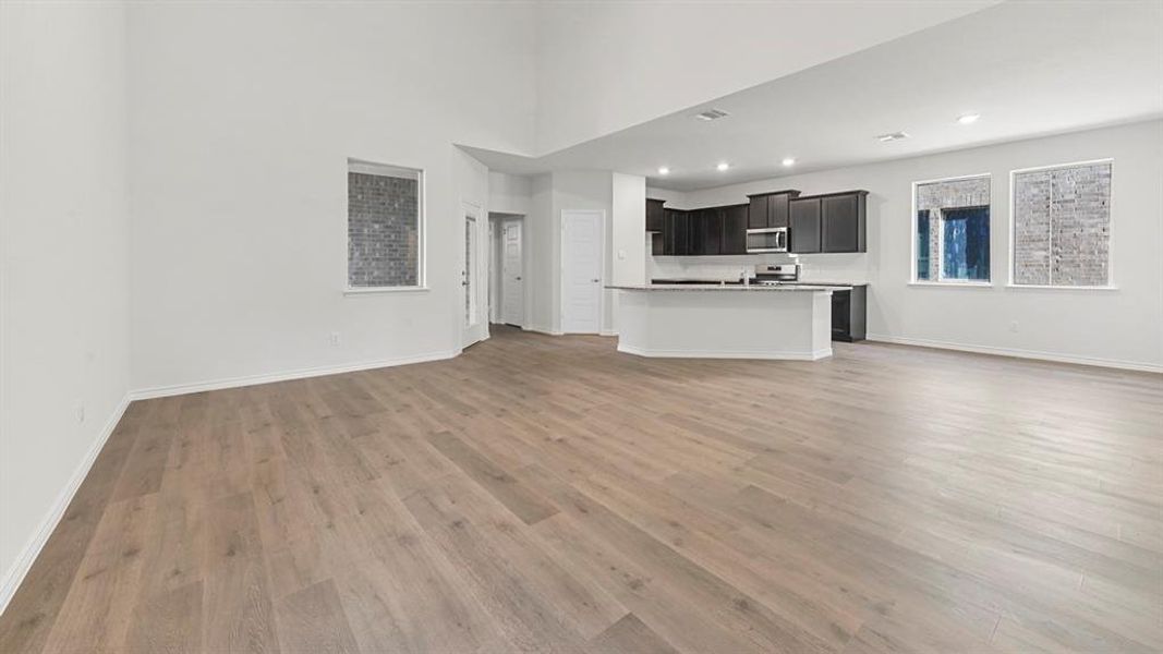 Unfurnished living room featuring light wood-style floors, recessed lighting, and a high ceiling