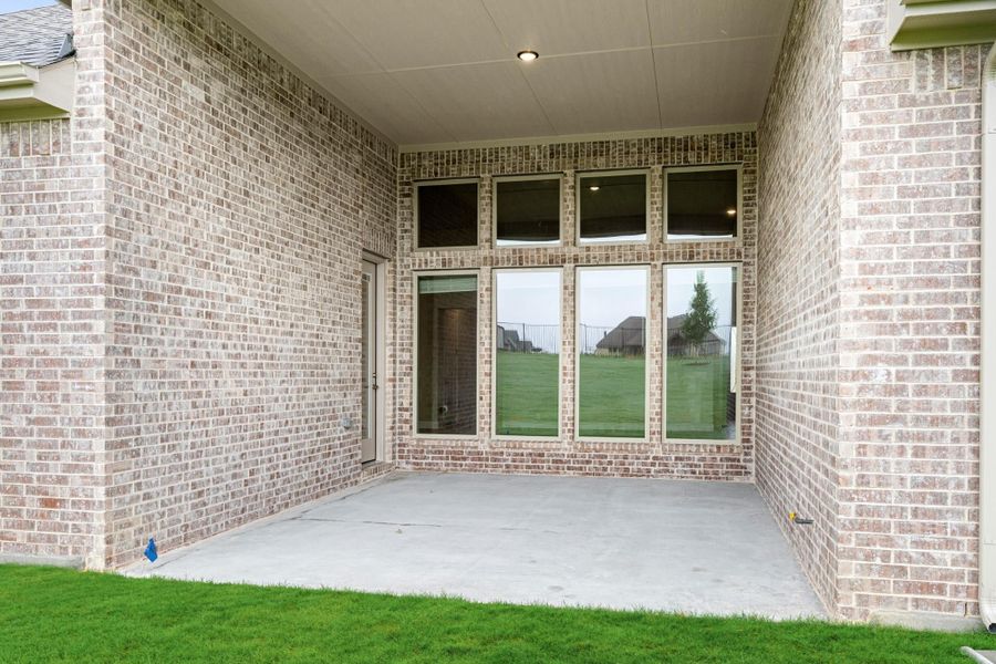 Covered back patio with concrete floor, brick exterior, and large windows overlooking a grassy yard