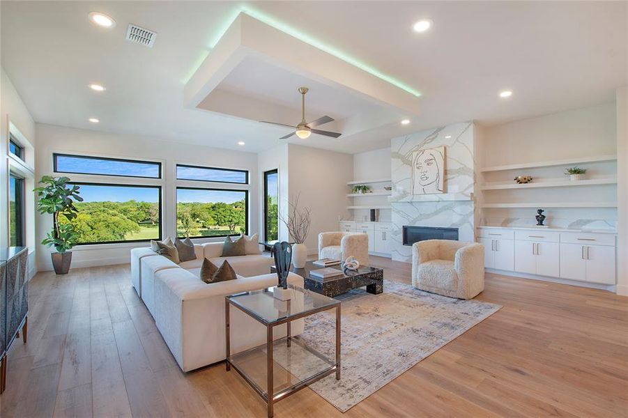 Living room with a premium fireplace, built in shelves, ceiling fan, and light hardwood / wood-style floors