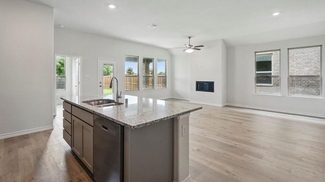 Kitchen featuring a glass covered fireplace, light stone countertops, stainless steel dishwasher, open floor plan, and an island with sink