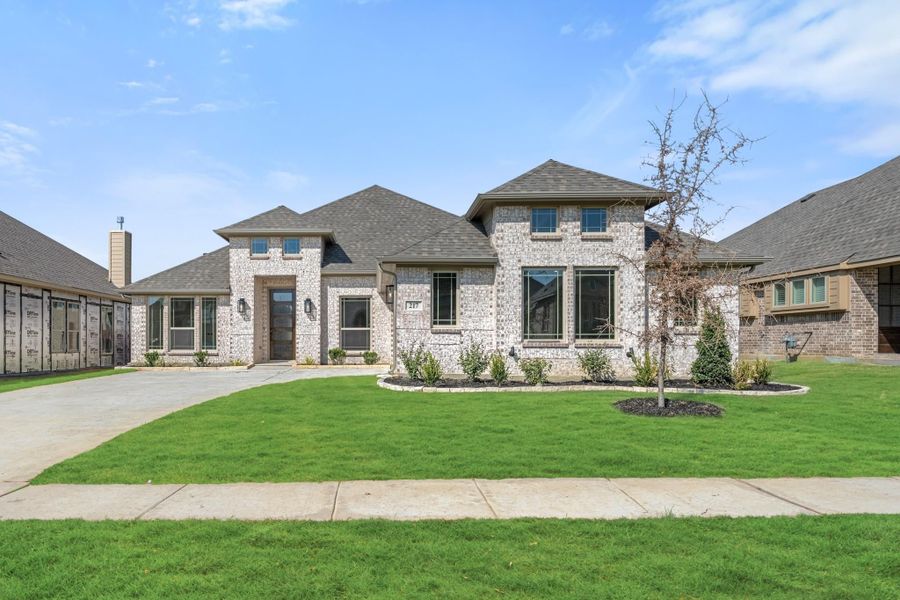 Two-story brick home with pitched roof, curved driveway, and manicured front lawn with landscaping