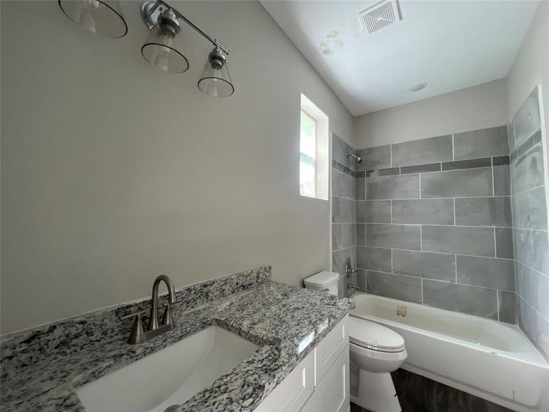 Full bathroom featuring vanity, tiled shower / bath combo, and toilet