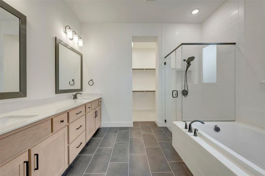 Spacious bathroom featuring a dual vanity with light wood-finish cabinetry and white countertops, a walk-in shower with a glass enclosure, a built-in soaking tub, and large format tile flooring Spacious bathroom featuring a dual vanity with light wood-finish cabinetry and white countertops, a walk-in shower with a glass enclosure, a built-in soaking tub, and large format tile flooring