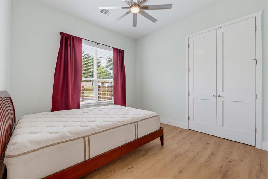 Sun-filled bedroom featuring elegant wood-look flooring and a functional ceiling fan for optimal comfort.