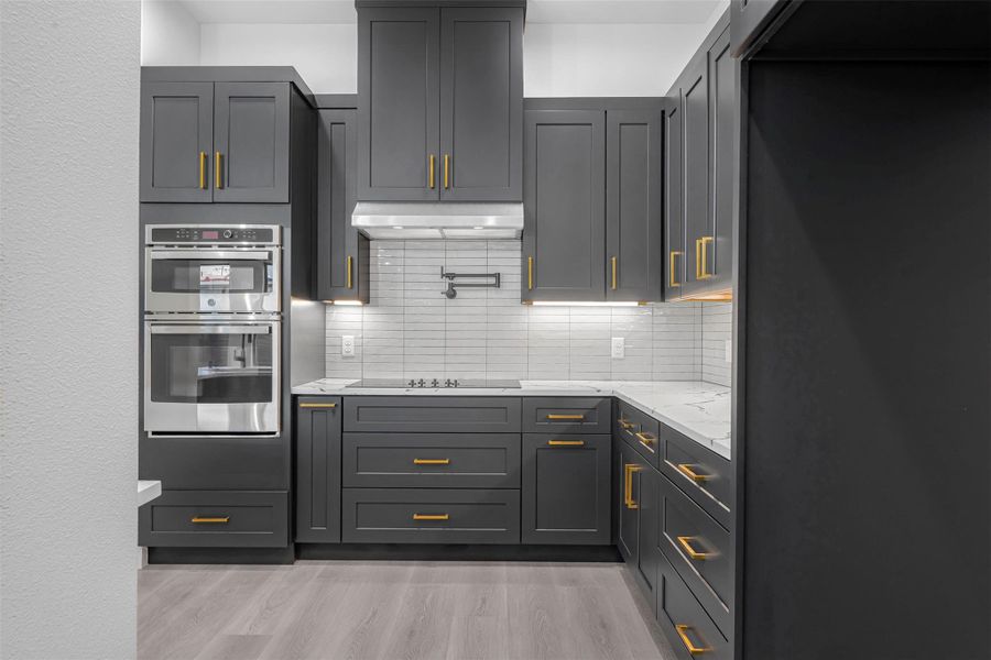 Kitchen featuring a double oven, under-cabinet range hood, light wood-finished floors, and a tasteful backsplash. Kitchen featuring a double oven, under-cabinet range hood, light wood-finished floors, and a tasteful backsplash.