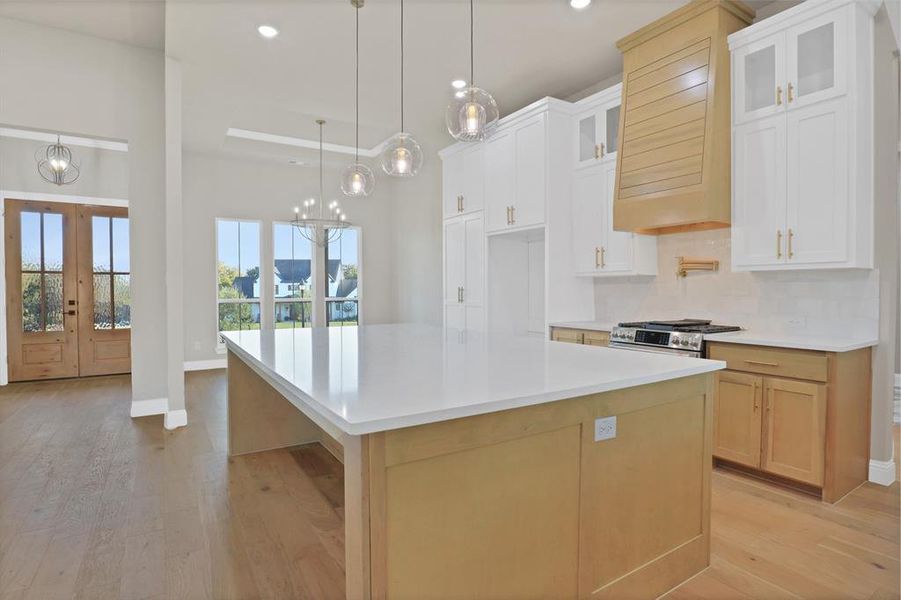 Kitchen with custom range hood, stainless steel range, white cabinets, and a spacious island