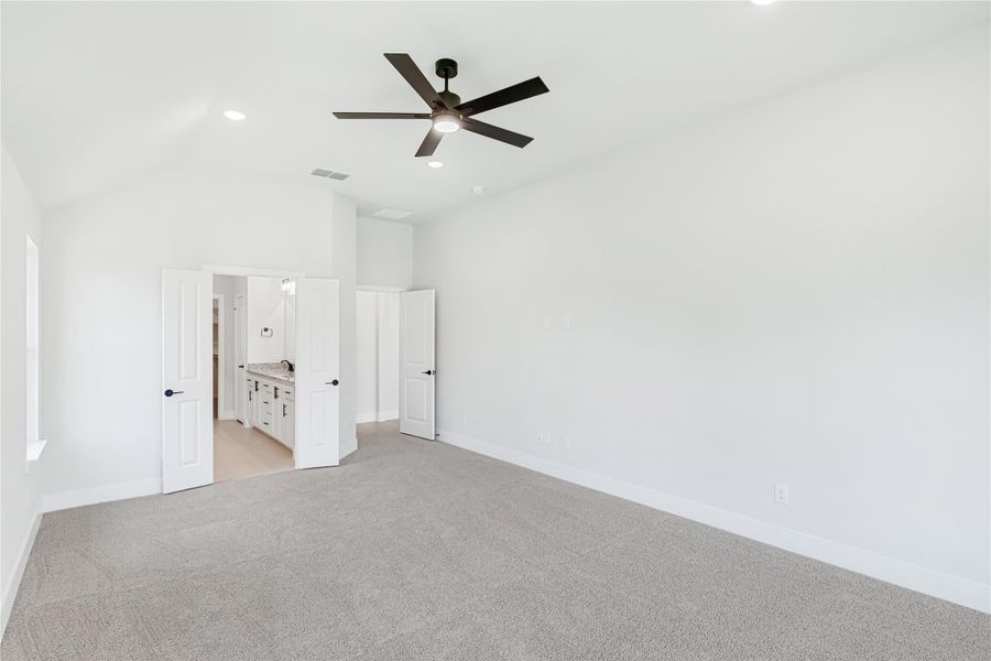 Empty master bedroom with gray carpet, ceiling fan, and ensuite bathroom entrance