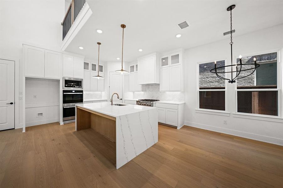 Kitchen featuring glass insert cabinets, white cabinetry, an island with sink, light stone counters, and decorative backsplash