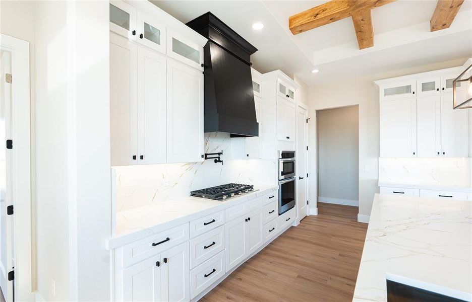 Kitchen featuring white cabinetry, light stone countertops, beamed ceiling, tasteful backsplash, and light wood finished floors