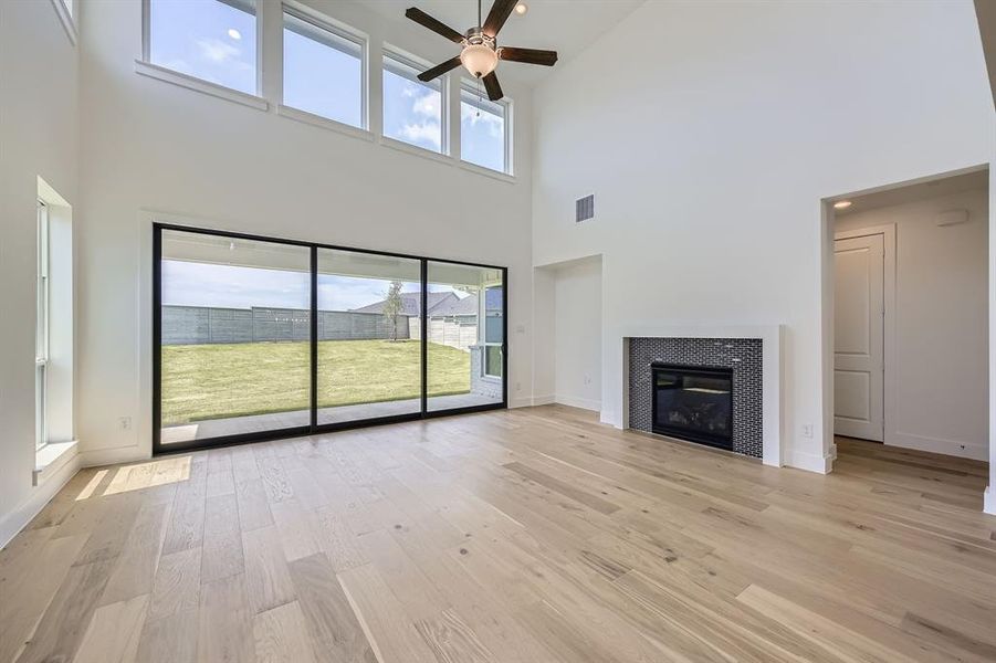Unfurnished living room featuring high vaulted ceiling, ceiling fan, light wood-style flooring, a tile fireplace, and baseboards Unfurnished living room featuring high vaulted ceiling, ceiling fan, light wood-style flooring, a tile fireplace, and baseboards