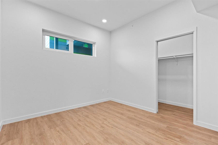 Unfurnished bedroom with a walk in closet, recessed lighting, a closet, light wood-style flooring, and baseboards