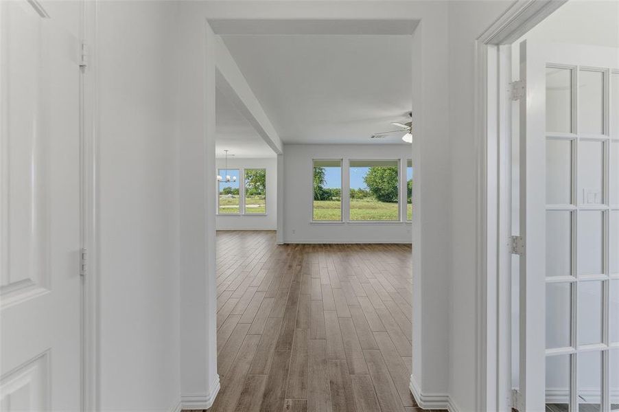 Hallway with wood-finish flooring, leading into an open living area featuring large windows, a ceiling fan, and a chandelier
