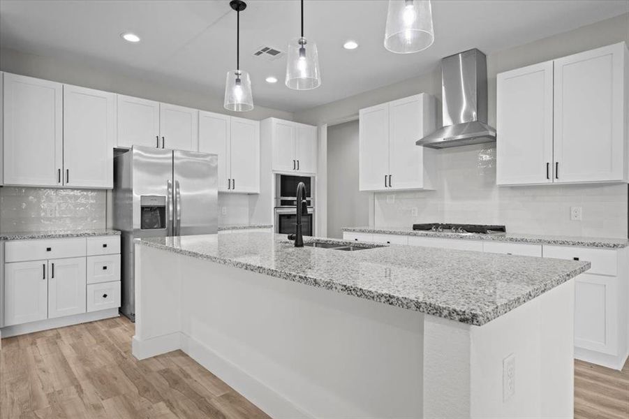 Kitchen featuring wall chimney range hood, stainless steel appliances, light wood-style floors, backsplash, and white cabinetry