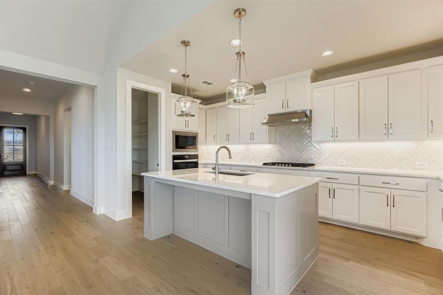 Kitchen featuring decorative backsplash, pendant lighting, an island with sink, white cabinetry, and light wood-style flooring