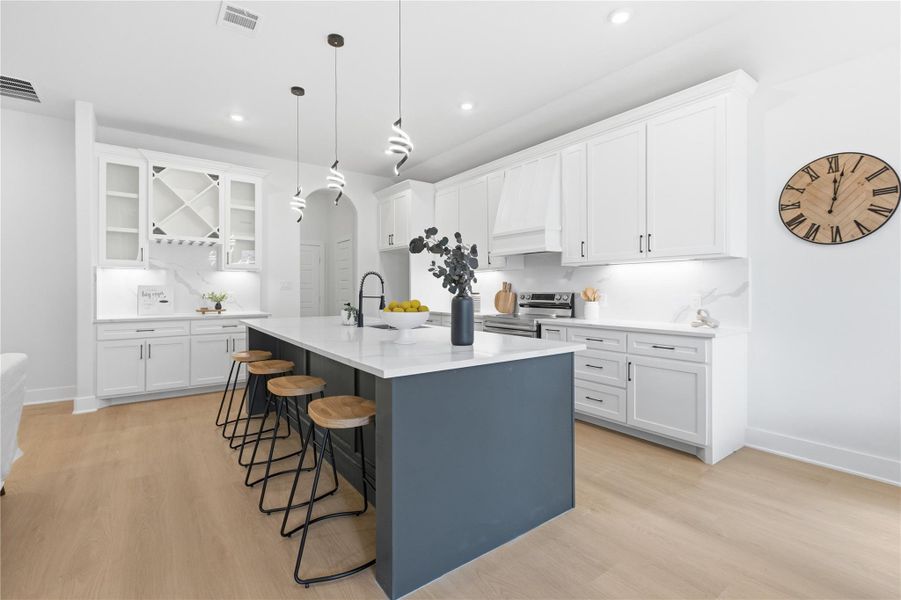 Two tone kitchen with two tone cabinetry, a kitchen breakfast bar, a kitchen island with sink, glass fronted cabinets, and light wood-style flooring