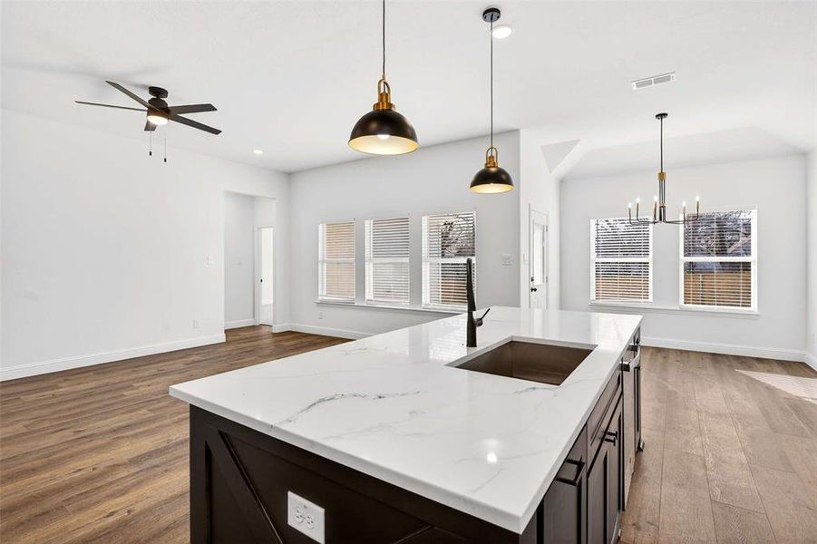 Kitchen with hanging light fixtures, a kitchen island with sink, dark wood-type flooring, dark cabinets, and recessed lighting