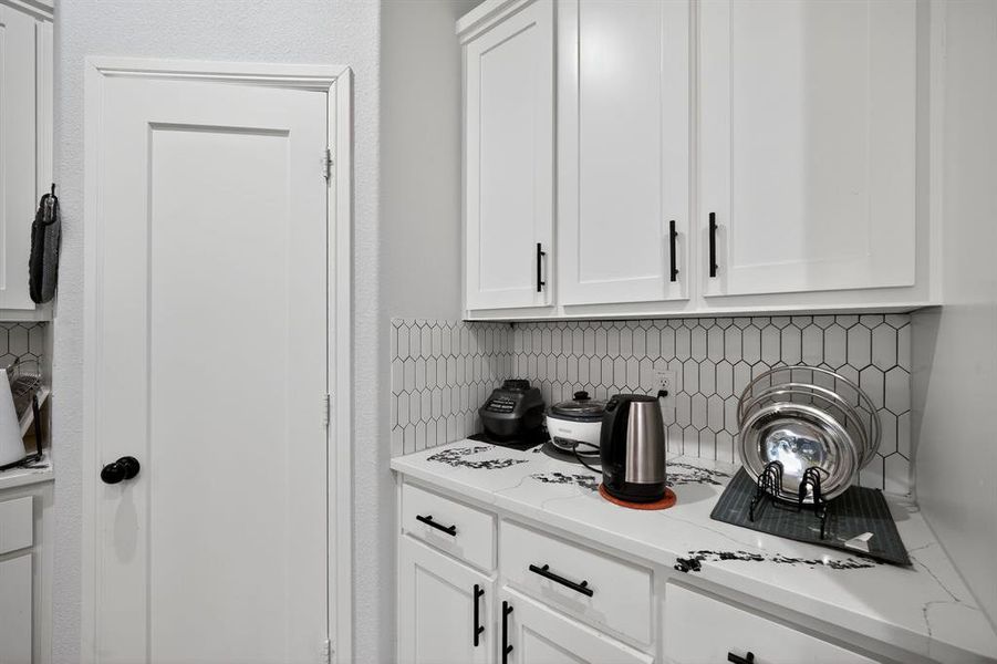 Bar area featuring decorative backsplash, white cabinets, and light countertops