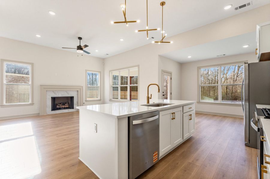 Kitchen featuring white cabinets, open floor plan, stainless steel appliances, a center island with sink, and suspended lighting