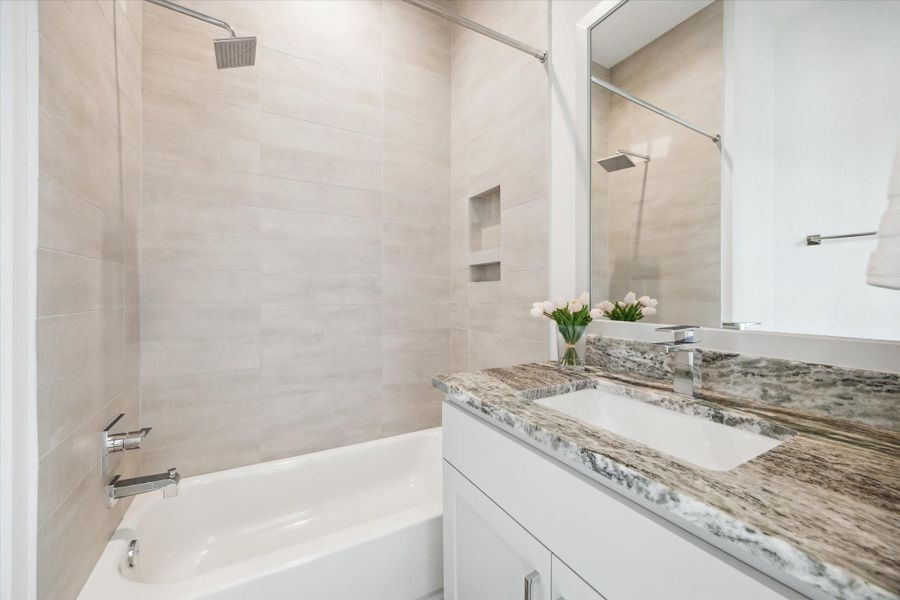 This bathroom features a modern design with a sleek white bathtub, neutral tiled walls, and a polished marble countertop. The built-in shelving adds convenience, and the large mirror enhances the space. Ideal for a contemporary home.