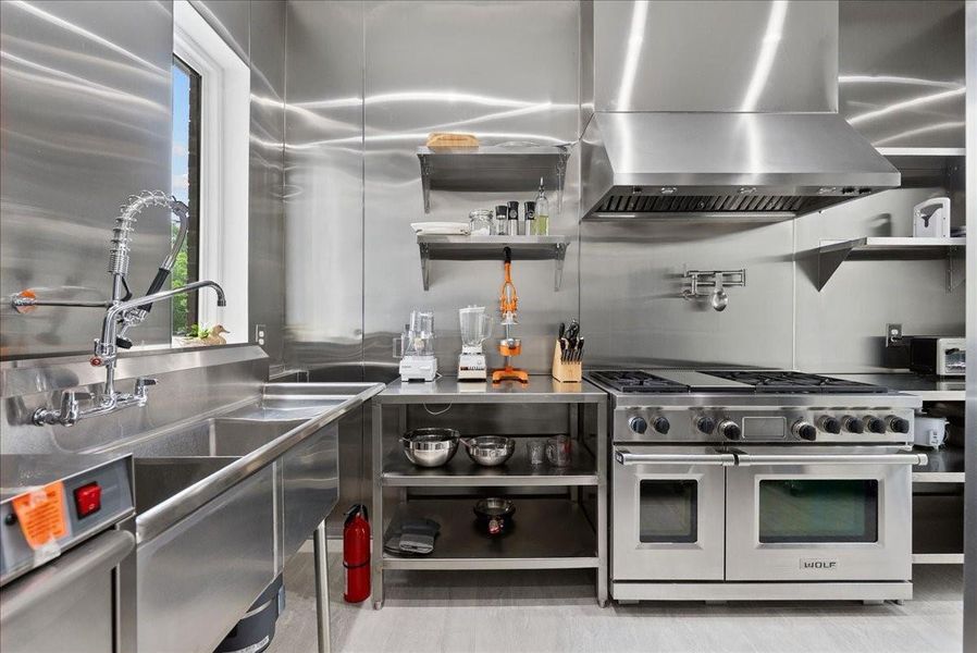 This commercial-grade secondary kitchen features floor-to-ceiling stainless steel, professional refrigeration, and a heavy-duty WOLF range.