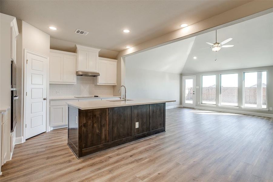 Kitchen with sink, white cabinets, lofted ceiling, tasteful backsplash, and a center island with sink Kitchen with sink, white cabinets, lofted ceiling, tasteful backsplash, and a center island with sink