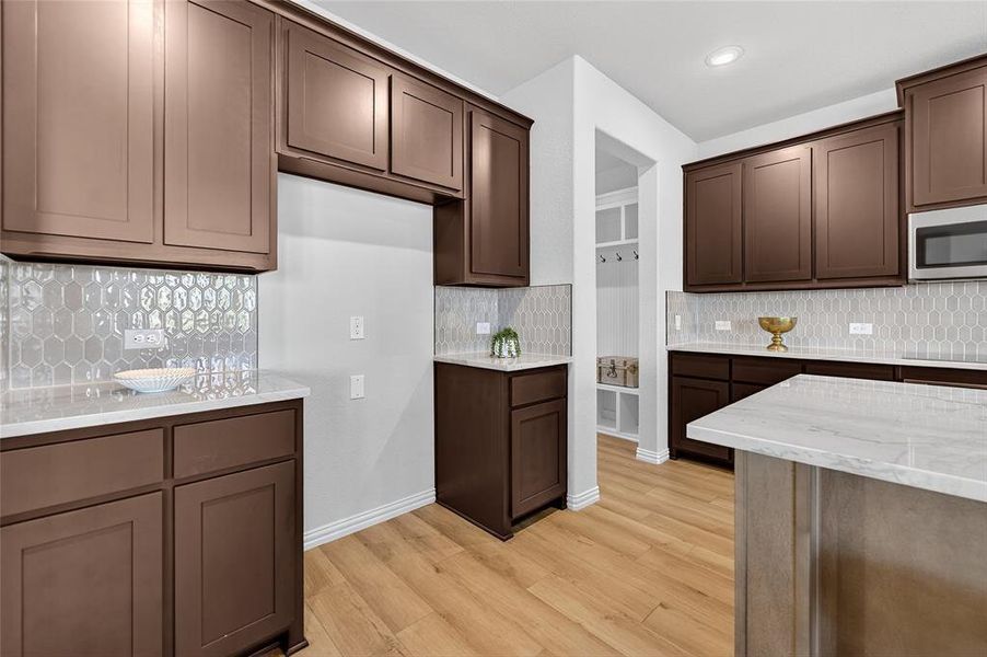 Kitchen featuring light stone countertops, light wood-type flooring, stainless steel microwave, dark brown cabinetry, and recessed lighting Kitchen featuring light stone countertops, light wood-type flooring, stainless steel microwave, dark brown cabinetry, and recessed lighting