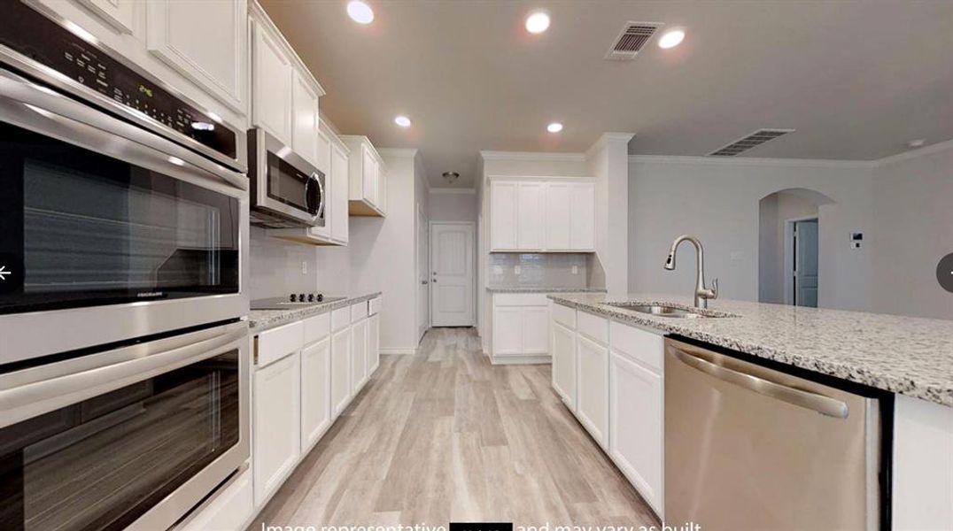 Kitchen featuring appliances with stainless steel finishes, a sink, arched walkways, light stone counters, and crown molding
