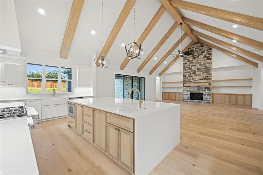 Kitchen with a stone fireplace, light wood-style flooring, beamed ceiling, high vaulted ceiling, and healthy amount of natural light