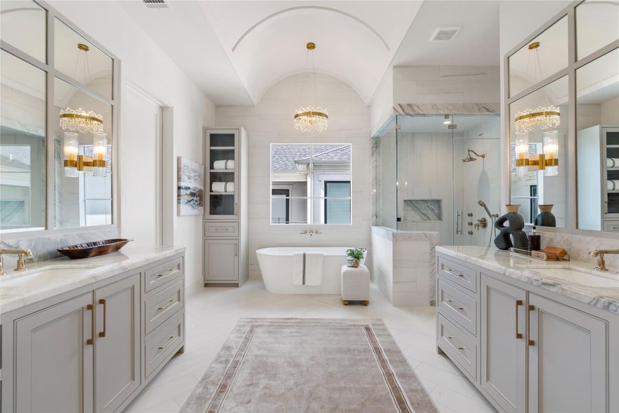 The pristine primary bath. A barreled ceiling adds height to the space, centered around the sumptuous soaking tub. Large-format porcelain tile lines the floor in a herringbone pattern for added dimension. The shower is encapsulated by Lisboa marble and features polished gold Brizo fixtures. Double vanities make sharing easy!