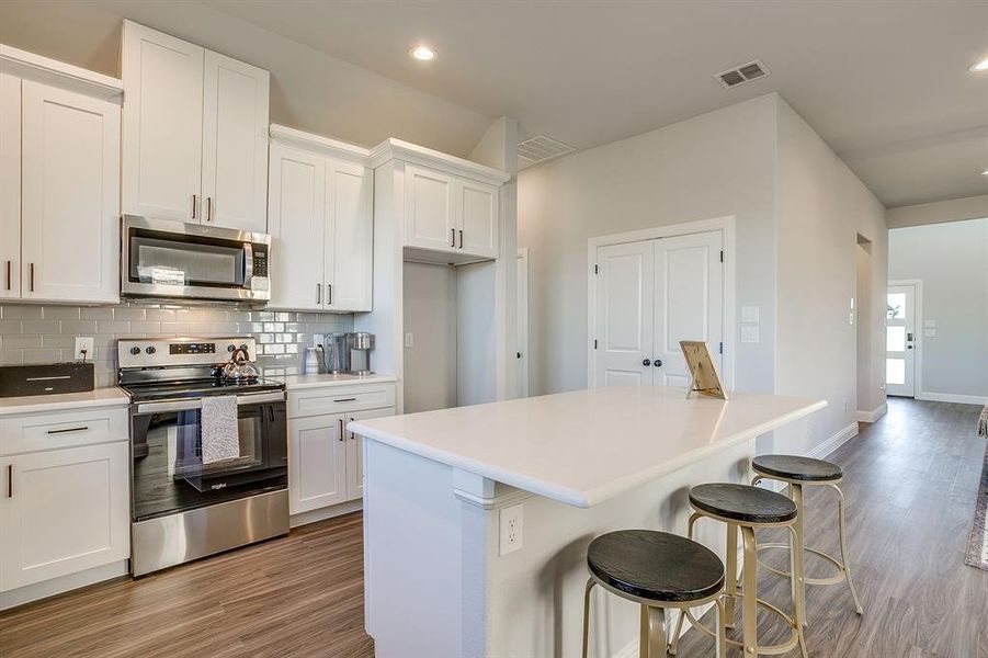 Kitchen featuring appliances with stainless steel finishes, a kitchen bar, white cabinets, a center island, and recessed lighting