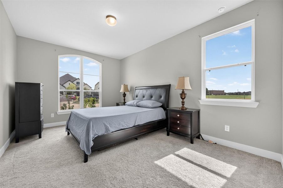 Bright secondary bedroom with plush carpeting and large windows showcasing peaceful neighborhood views. The neutral palette and natural light create a warm, welcoming atmosphere.