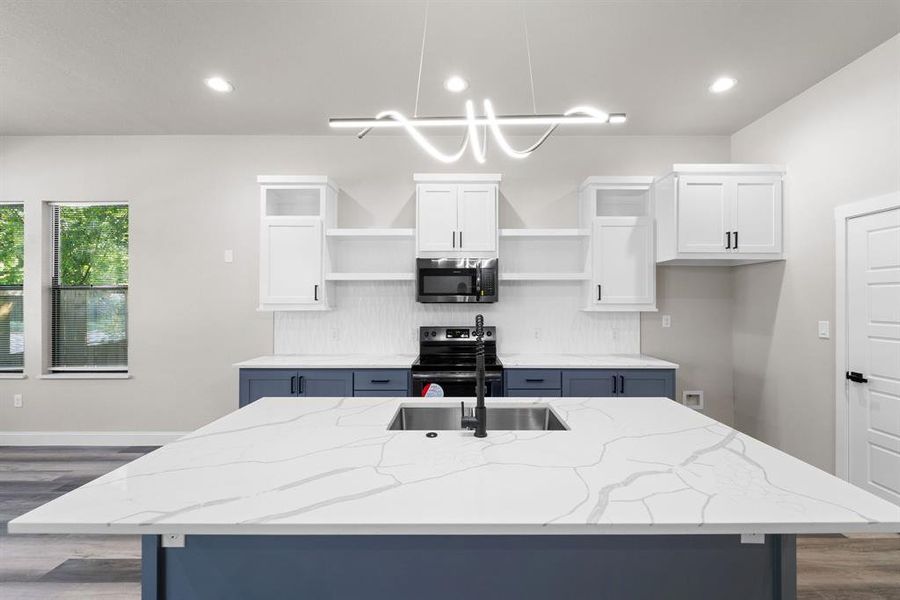 Kitchen with light stone counters, white cabinets, an island with sink, decorative light fixtures, and black range with electric cooktop