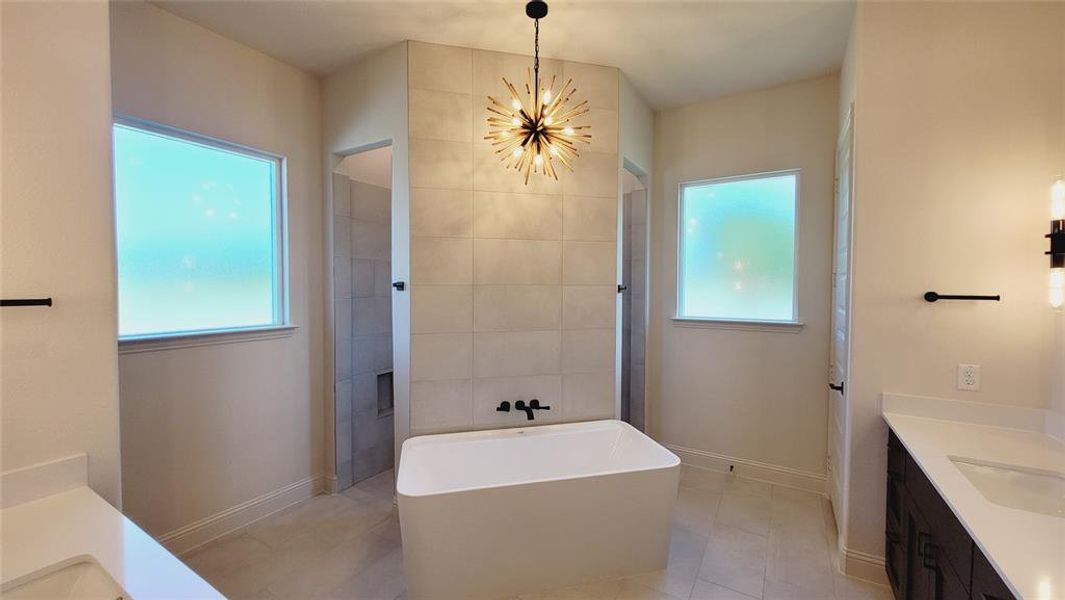 Freestanding soaking tub with dark-finish wall-mounted fixtures, dual vanity sinks with quartz countertops, and a central sputnik-style chandelier