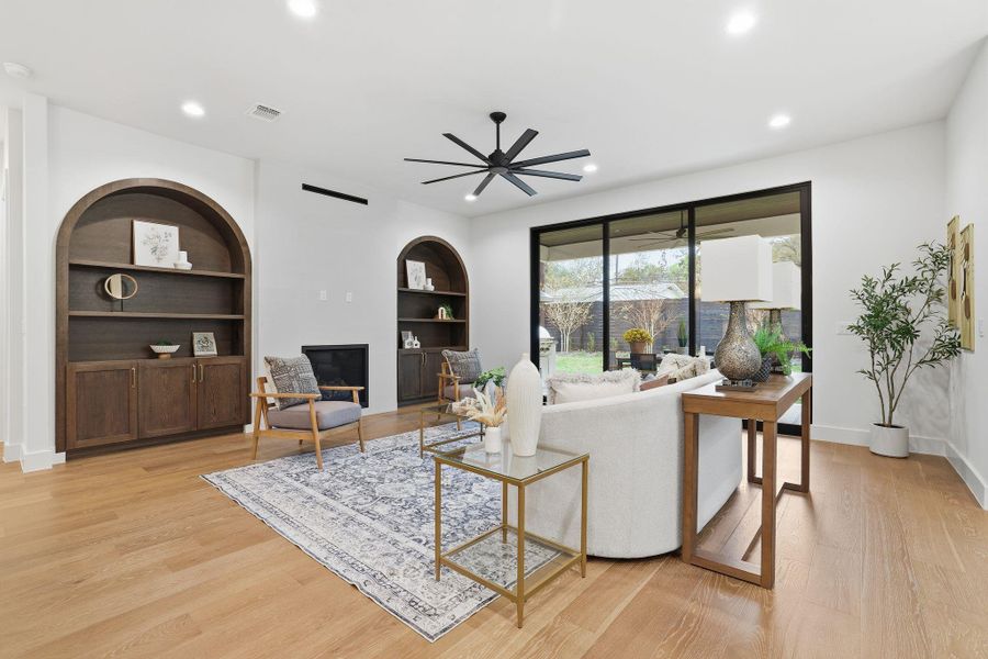 Living room with built in features, light wood-style flooring, recessed lighting, ceiling fan, and a glass covered fireplace