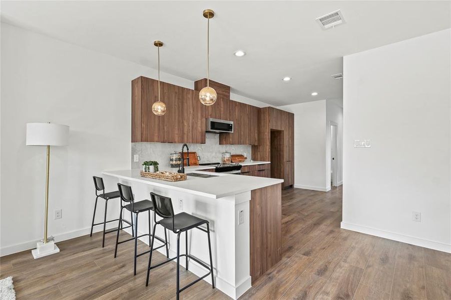 Kitchen featuring a breakfast bar, sink, hanging light fixtures, kitchen peninsula, and stainless steel appliances