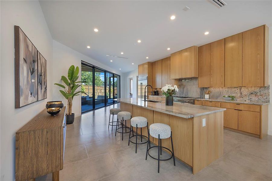 Kitchen with sink, backsplash, a large island, light stone counters, and a breakfast bar