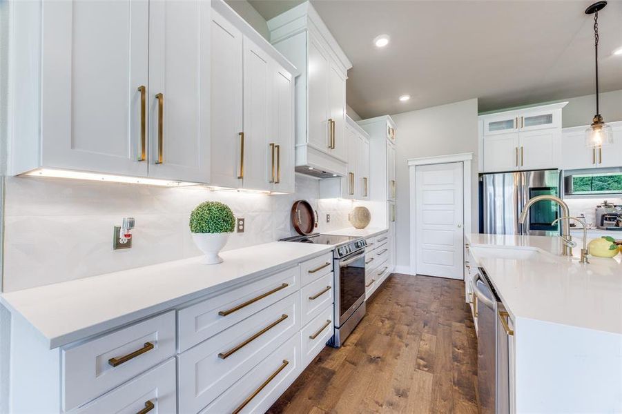 Kitchen featuring tasteful backsplash, appliances with stainless steel finishes, hanging light fixtures, white cabinets, and light stone countertops