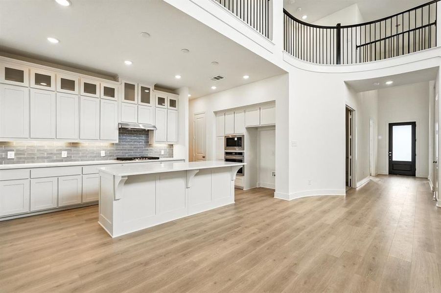 Kitchen featuring a towering ceiling, a kitchen island, backsplash, a breakfast bar, and recessed lighting Kitchen featuring a towering ceiling, a kitchen island, backsplash, a breakfast bar, and recessed lighting