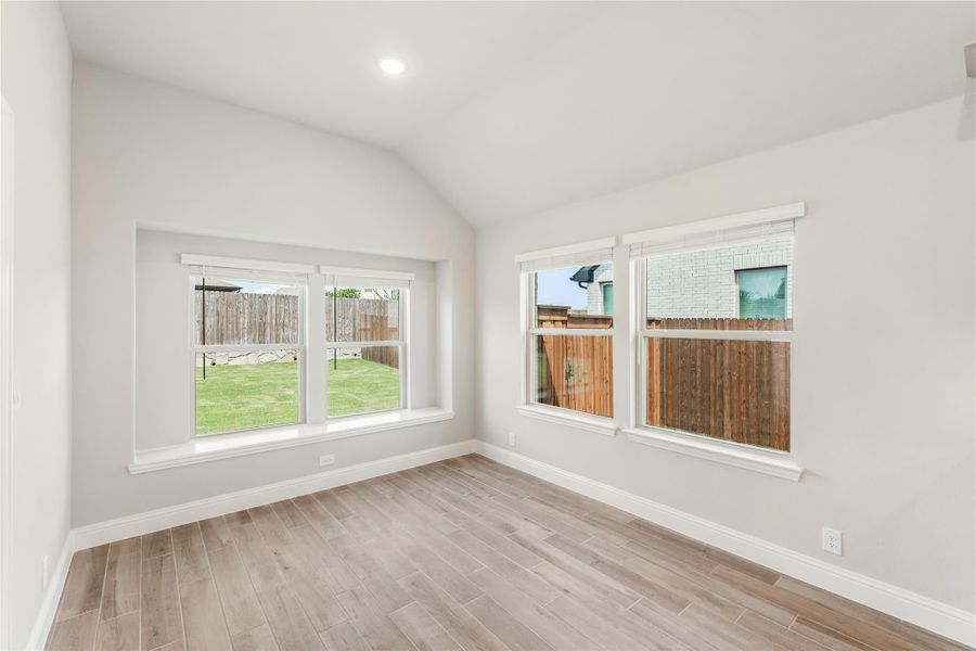 Empty room with vaulted ceiling, wood-look floors, and multiple windows overlooking a fenced backyard
