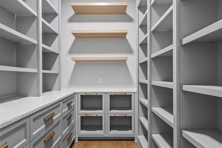 Offering exceptional storage and organization, the walk-in pantry is thoughtfully designed with Opal White marble counters for a refined yet functional workspace. Custom-built cabinetry pairs beautifully with floating white oak shelves, while metal mesh front drawer storage adds a stylish touch. The warm white oak hardwood floors complete the space, creating a seamless blend of elegance and practicality.