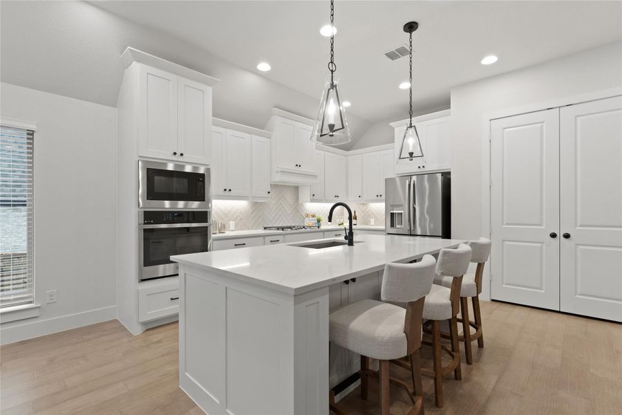 Contemporary kitchen featuring white cabinetry, light wood-finish flooring, a central island with countertop seating, stainless steel appliances, and pendant lighting
