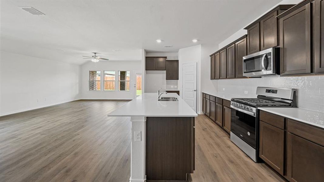 Open-concept kitchen and living area featuring wood-finish flooring, white countertops, dark wood cabinetry, a stainless steel range, and a ceiling fan in the living space