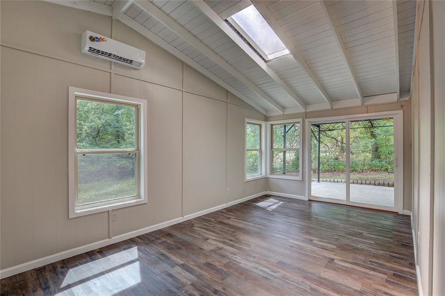 Unfurnished room featuring wood-type flooring, lofted ceiling with skylight, a wall unit AC, and a healthy amount of sunlight