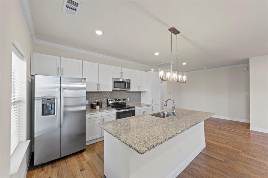 Kitchen with crown molding, stainless steel appliances, decorative light fixtures, light wood-type flooring, and white cabinets