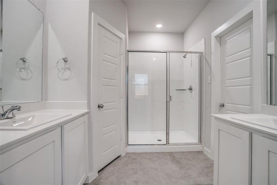 Bathroom featuring two vanities, a shower stall, and light tile patterned flooring