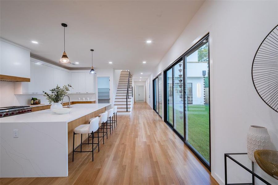 Kitchen featuring an island with sink, light wood-type flooring, hanging light fixtures, white cabinetry, and light stone countertops