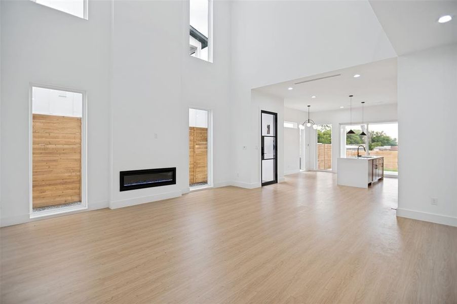 Spacious open-concept living area featuring light wood-finish flooring, a contemporary linear fireplace, and abundant natural light from multiple windows