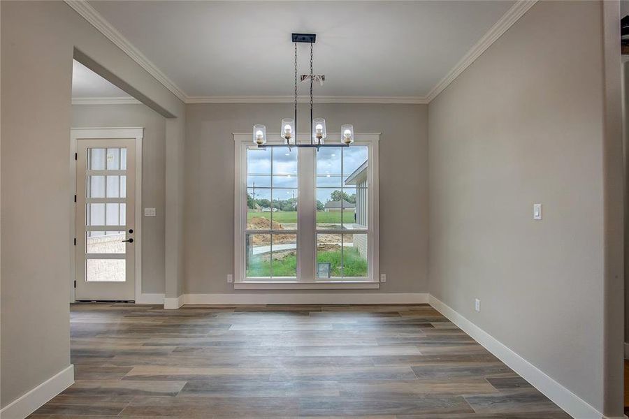Unfurnished dining area featuring ornamental molding, an inviting chandelier, and wood-type flooring Unfurnished dining area featuring ornamental molding, an inviting chandelier, and wood-type flooring